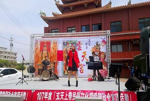 這張「舞臺表演」的照片是，一個歌手在舞臺上唱歌，旁邊還有樂團伴奏，舞臺背景是紅色布幕，寫著「慶天宮」。