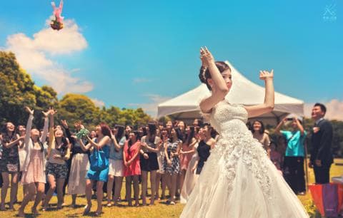 這張婚禮的照片是一對新人正在拋捧花，新娘穿著白色婚紗，新郎穿著西裝，圍繞著他們的是賓客，大家都在歡笑和祝福他們。