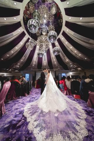 這張「婚禮」的照片是一對新人站在紫色的地毯上，新娘穿著白色婚紗，新郎穿著西裝，他們正準備步入禮堂。