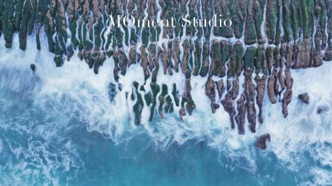 這張「海邊岩石」的照片是，佈滿綠色海藻的岩石從高處往下延伸，海浪拍打在岩石上，形成白色泡沫，畫面呈現出大自然的壯麗景色。