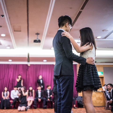 這張「舞廳」的照片是 一對情侶正在跳舞，男的穿著西裝，女的穿著禮服，背景是一群人。