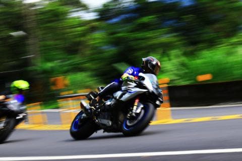 這張「摩托車比賽」的照片是，一位車手騎著賽車，在蜿蜒的道路上高速前進，背景是模糊的樹木，畫面充滿了速度感和刺激感。