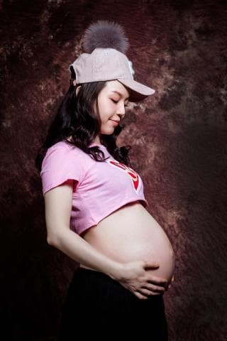 這張照片是一個懷孕的婦女。她穿著粉紅色的短袖上衣，戴著帽子，肚子很大，顯然已經懷孕很久了。