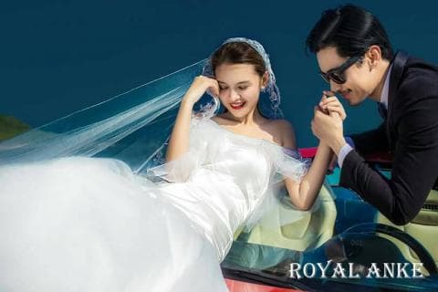 這張照片是一對新人在車上擁抱的照片，新娘穿著白色婚紗，新郎穿著黑色西裝，新娘的頭紗覆蓋在她的頭上，新郎正輕輕地吻著新娘的手。