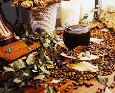 這張「咖啡與葉子」的照片是一杯黑咖啡，旁邊散落著許多咖啡豆和綠色的葉子。