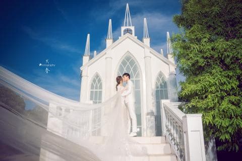這張照片是一對新人正在教堂前親吻，背景是白色的教堂和綠色的樹木，充滿著幸福浪漫的氣氛。