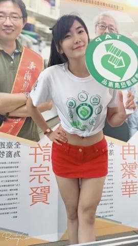 這張照片是一個年輕女子站在街頭，她穿著白色T恤和紅色短裙，手上拿著一個綠色圓形標誌。