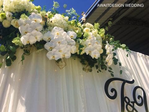 這張照片是一對新人婚禮的佈置，照片中最重要的是用白色花朵裝飾的拱門。花朵中以白色蘭花為主，襯託著其他綠葉，營造出浪漫的氛圍。
