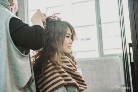 這張照片是一個女子在梳頭，她的髮型師正在幫她整理頭髮。女子長長的頭髮很漂亮，她正看著窗戶外。