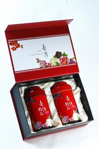 這張照片是兩個紅色的錫罐，罐子上印著精美的中國風圖案，被放在一個紅色的盒子裡。