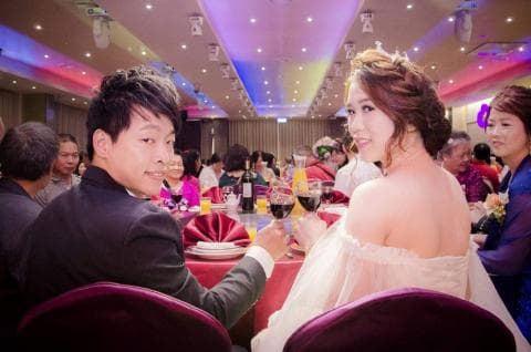 這張婚禮的照片是新郎和新娘在婚宴上舉杯祝酒，背景是熱鬧的婚宴現場。