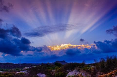 這張「日落」的照片是夕陽餘暉穿透雲層，照亮天空，形成一道道光束，畫面充滿了溫暖和希望。