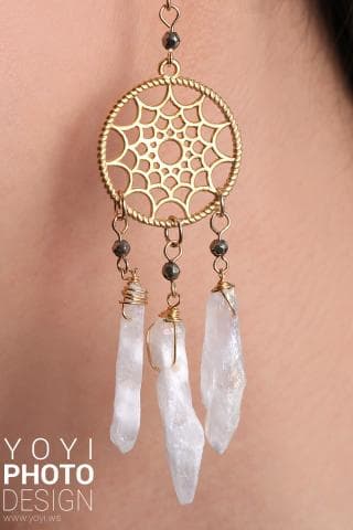 這張「捕夢網耳環」的照片是一個金色圓形捕夢網，上面有精緻的網狀圖案，下方垂吊著三個白色水晶，整體設計精美，非常適合女性佩戴。