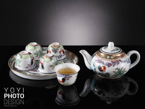 這張照片是 一套精美的陶瓷茶具，包括一個茶壺和四個茶杯，茶壺上繪有精緻的花卉和鳥類圖案，茶杯則以簡單的圖案裝飾。茶壺和茶杯都呈現出優雅的白色，與背景形成鮮明對比。