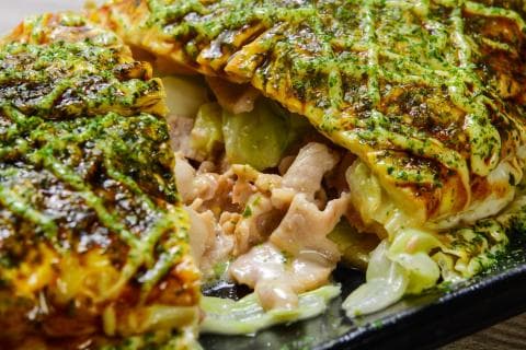 這張「大阪燒」的照片是兩塊煎得金黃的餅皮，中間夾著滿滿的肉絲、高麗菜和醬汁，看起來非常美味。
