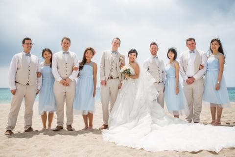 這張照片是一對新人和他們的伴郎伴娘在沙灘上舉行婚禮，新娘穿著優雅的婚紗，笑容燦爛，新郎則穿著筆挺的西裝，與新娘深情對望。