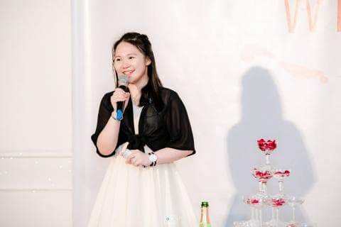 這張照片是一個年輕女子手持麥克風，正在發表演講。