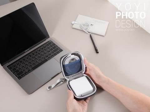 這張「電子產品收納包」的照片是，一個深藍色的收納包裡放著一個白色充電器和一條白色線。旁邊還有一臺銀色的筆電。