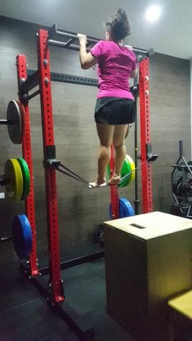 這張照片是一名女性在健身房使用懸吊訓練器材進行訓練。她雙腳站在訓練器材上，雙手握住上方橫桿，身體懸空。