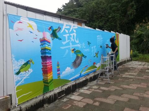 這張照片是一幅大型的壁畫，壁畫上畫著五顏六色的建築物、鳥類和樹木，背景是一片藍天白雲。