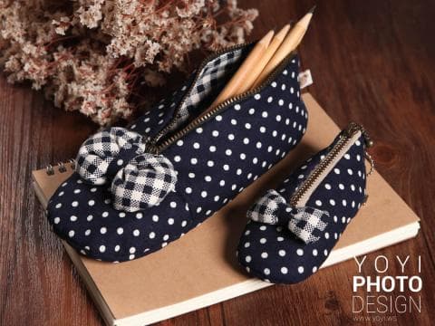 這張照片是兩個用藍色布料製作的筆袋，上面佈滿白色圓點，筆袋上還有一個白色格子的蝴蝶結裝飾。