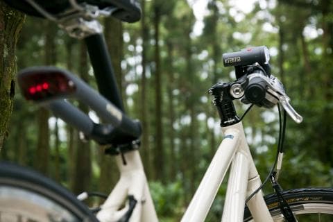 這張照片是一輛白色自行車，車子前面有一個裝在車把上的紅色小燈，車架上有一個黑色的座椅，車子後輪的旁邊有一個黑色的後照鏡。