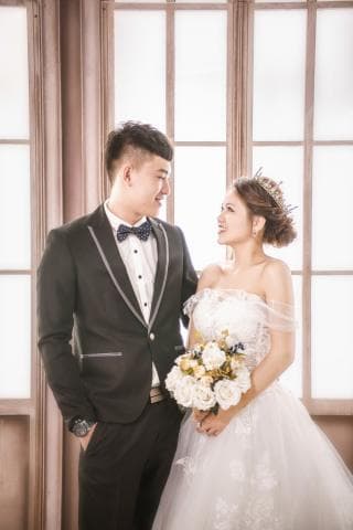 這張照片是一對新人在婚禮當天拍攝的婚紗照，照片中，新郎穿著黑色西裝，新娘穿著白色婚紗，他們手牽著手，新郎深情地注視著新娘，新娘也露出幸福的笑容，畫面充滿了浪漫和幸福。