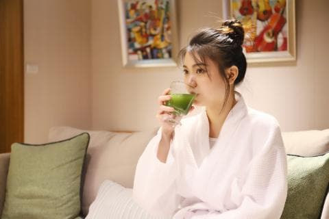 這張「一位女子坐在沙發上，穿著白色浴袍，手裡拿著一杯綠色飲料」的照片是。