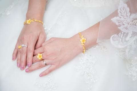 這張照片是一對戴著金飾的雙手，其中一隻手上戴著三枚戒指，另一隻手上戴著兩條金手鍊，看起來像是婚禮的場景。
