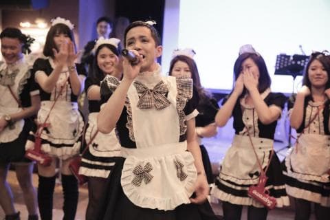 這張「一群人穿著女僕裝」的照片是一個男的站在一群穿著女僕裝的女生中間，他拿著麥克風，看起來像是正在唱歌。