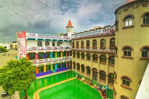 這張「兒童遊樂場」的照片是，一個有城堡和遊樂設施的兒童遊樂場，周圍有許多綠色的植物和樹木。