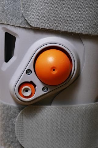 這張「護踝」的照片是一個橘色的圓形按鈕，按鈕上有一個小孔，周圍有灰色和白色的塑膠。