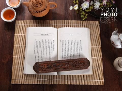 這張照片是一本打開的書放在竹蓆上，書上放著一個精緻的木雕盒子。