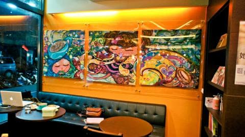 這張「咖啡廳」的照片是一個有牆上裝飾藝術的咖啡廳，以及兩張桌子和椅子。