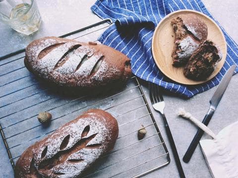 這張「兩條麵包和一些切片的麵包」的照片是兩條新鮮出爐的麵包，一條放在鐵架上，另一條放在木盤上。