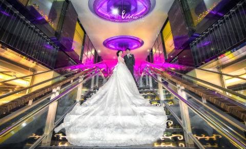 這張照片是一對新人站在自動扶梯上，新郎穿著西裝，新娘穿著白色婚紗，他們看起來很幸福。
