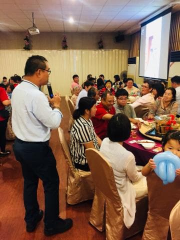 這張照片是一個家庭聚餐的場景，照片中有一位男士正在臺上講話，他拿著麥克風，看起來很投入。