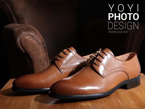 這張照片是兩雙棕色皮鞋，放在木地板上，其中一雙放在另一雙的前面，光線打在皮鞋上，讓皮鞋看起來非常有光澤。