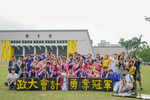 這張「一群人站在體育館前，手舉著標語」的照片是一群人在體育館前，舉著寫著「政大會計勇奪冠軍」的標語，歡慶勝利。