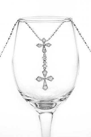 這張照片是一個鑲滿鑽石的十字架項鍊，掛在一個透明的酒杯上。