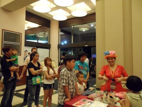 這張「一群人聚會」的照片是，一群朋友和家人在一個明亮的房間裡，他們正在交談和玩耍。照片中有一位女士戴著氣球帽，她在和一個小孩玩遊戲，其他的人則在旁邊觀看。