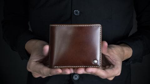 這張照片是一個男人拿著一個深棕色的皮革錢包。錢包的邊緣是白色的縫線，看起來很精緻。