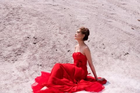 這張照片是一個穿著紅色禮服的女子坐在白色沙灘上。