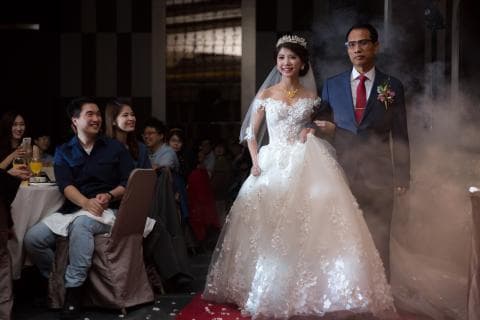 這張婚禮照片是一對新人正在舉行婚禮，新娘穿著美麗的婚紗，新郎穿著西裝，他們手牽著手，笑容滿面，非常幸福。