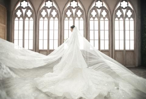 這張照片是一個穿著婚紗的新娘，她站在一個有著拱形窗戶的房間裡。她的婚紗很長，拖在地上，看起來很優雅。