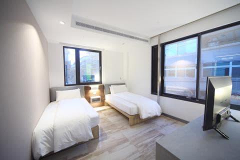 這張「現代簡約風格」的照片是一間臥室，房間裡有兩張雙人床，一張靠近窗戶，另一張靠近牆壁。房間還有個電視和一張床頭櫃。