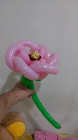 這張照片是一朵用氣球做的粉紅色玫瑰，玫瑰花瓣中間放了一顆金色的巧克力。