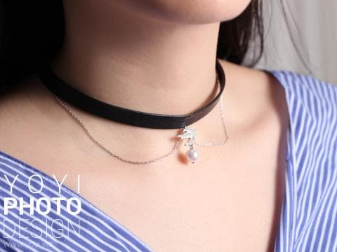 這張「項鍊」的照片是一個戴著黑色皮革項鍊和銀色珍珠項鍊的女生，她穿著藍白條紋襯衫。