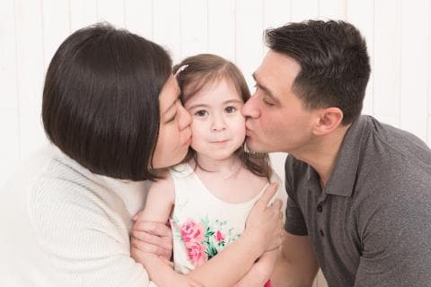 這張照片是一對父母親親吻他們可愛的女兒，展現出滿滿的愛與溫暖。