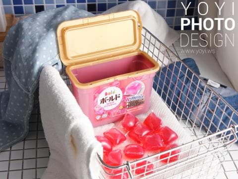 這張照片是一些紅色洗衣膠囊，放在一個金屬籃子裡，旁邊放了一罐洗衣精。